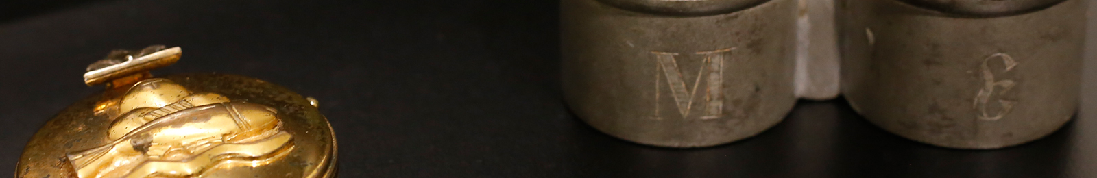 Cropped close-up of a round golden container carved with designs and two round silver containers joined together.