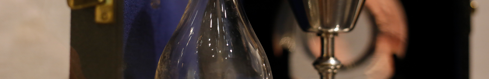 Cropped close-up on a blown-glass vessel, the stem of a silver chalice, and a silver plate in the background