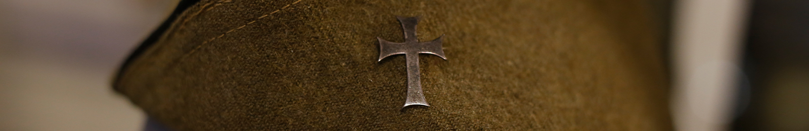 Cropped close-up on a wool olive-green military cap with a cross pinned to it.