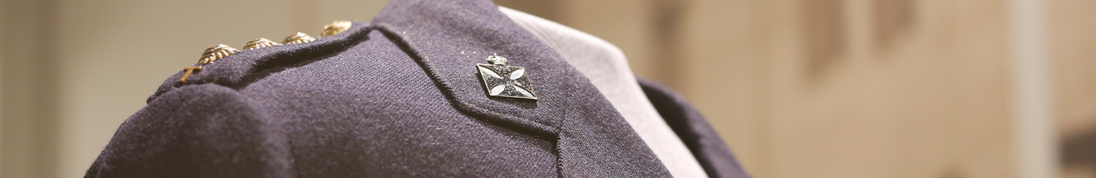 Cropped close-up on the collar and shoulders of a navy-blue uniform tunic with metal insignias pinned to both.